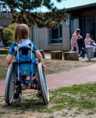 Kind im Rollstuhl vor einer Schule